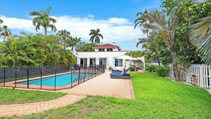 Una propiedad residencial con piscina, patio trasero cercado y una casa con techo rojo.