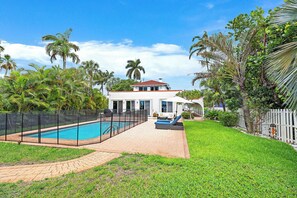Una propietat residencial amb piscina, un pati tancat per una tanca i una casa amb teulada vermella.