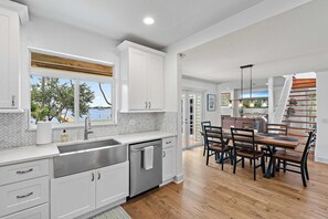 A kitchen with a large window, a dining area with a wooden table and chairs, and a staircase leading to another level. - Intracoastal Vista II – 3BR Waterfront Escape with Private Boat Dock! (Lantana)
