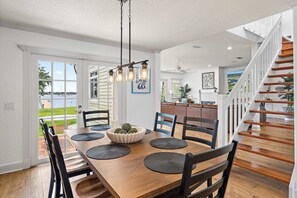 A dining area with a wooden table, black chairs, a bowl of decorative balls, and a hanging light fixture. - Intracoastal Vista II – 3BR Waterfront Escape with Private Boat Dock! (Lantana)