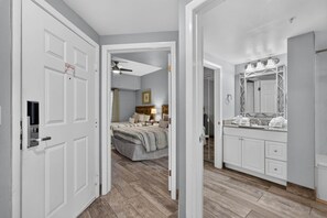 Ein Schlafzimmer mit Bett, Nachttischen, Deckenventilator und einem Badezimmer mit Waschbecken, Spiegel und Handtuchhalter.
