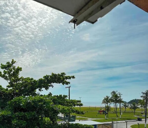 Blick aus einem Flugzeugfenster auf Strand, Palmen und eine Wiese mit Zaun.