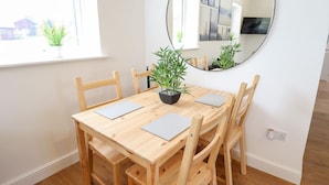 Un comedor con una mesa de madera, cuatro sillas, dos plantas en macetas, un espejo redondo y una ventana con vistas.