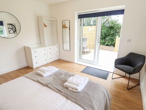 Ein Schlafzimmer mit einem Bett, einer Kommode, einem Sessel, einem großen Spiegel und einer Schiebetür zum Außenbereich.