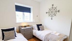 Un dormitorio con dos camas, una mesita de noche, un adorno de pared con brújula y una ventana con persiana oscura.