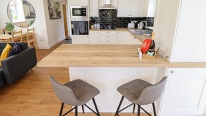 Una cocina moderna con armarios blancos, salpicadero negro y encimera de madera. Se ven dos taburetes de bar en primer plano.