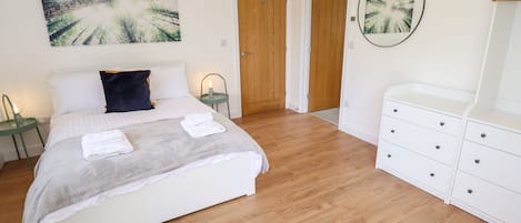 Un dormitorio con cama, mesita de noche, cómoda y dos puertas.