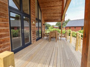 A wooden deck with a table and chairs, large windows, and a view of surrounding buildings. - The Lilac Owl (Lincoln)