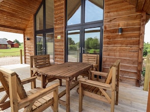 A wooden cabin with a large table and chairs, a covered patio, and large windows. - The Lilac Owl (Lincoln)