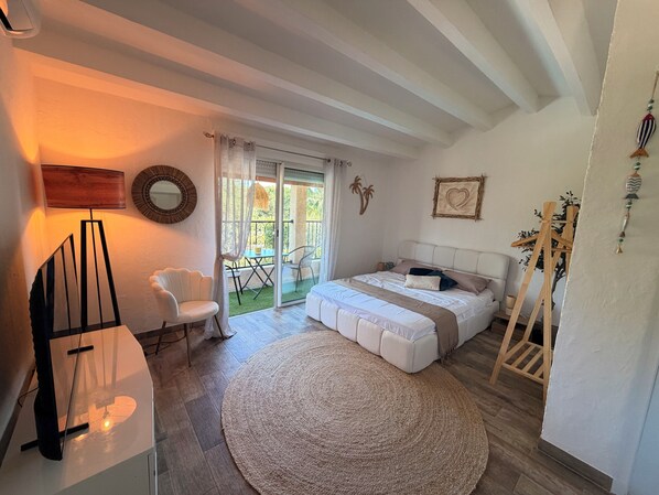 Ein Schlafzimmer mit Bett, Stuhl, Schreibtisch, Lampe, einem runden Teppich und einem Balkon mit Tisch und Stühlen.