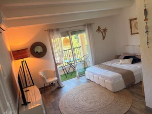 Ein Schlafzimmer mit Bett, Sessel, Lampe, einem runden Teppich und einem Balkon mit Tisch und Stühlen.