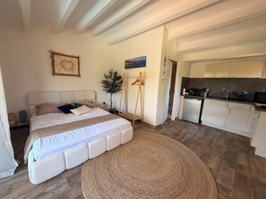 Ein Schlafzimmer mit Bett, Nachttisch und Zimmerpflanze. Es gibt eine Küchenzeile mit Spüle und Schränken.