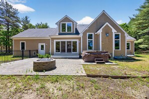 A two-story house with a brick exterior, a front porch, a stone fire pit, and a hot tub. - Contemporary 3BR House: New Furniture, AC, Hot Tub, 2Gbps Wi-Fi & Pet-Friendly (Falmouth)