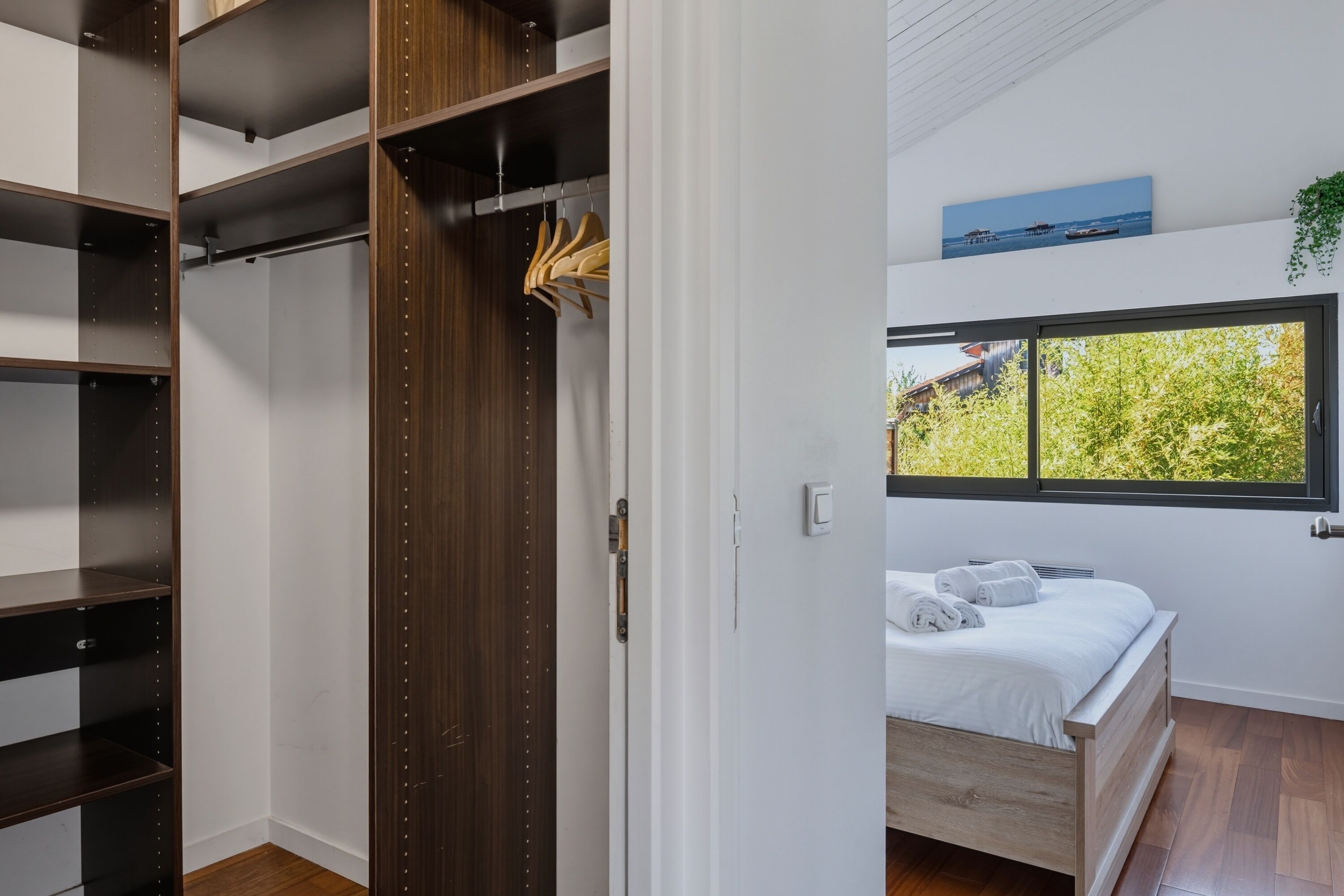 Un dormitorio con cama, ventana con vistas a la vegetación, armario con estantes y una percha.