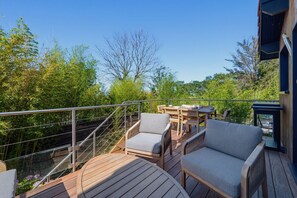Een houten terras met tuinmeubilair, een metalen hekwerk en uitzicht op bomen en groen.