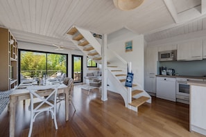 Ein modernes Interieur mit einer Holztreppe, einem Essbereich mit Blick ins Freie und einer Küche mit weißen Schränken.