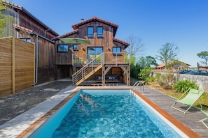 Ein Holzhaus mit Swimmingpool, einer überdachten Terrasse und einer Treppe zu einem Balkon.