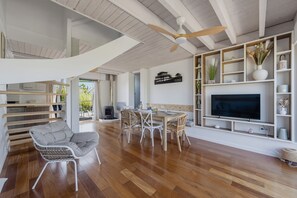 Een ruime woonkamer met houten vloer, witte meubels, een plafondventilator en een televisie op een wit plank.