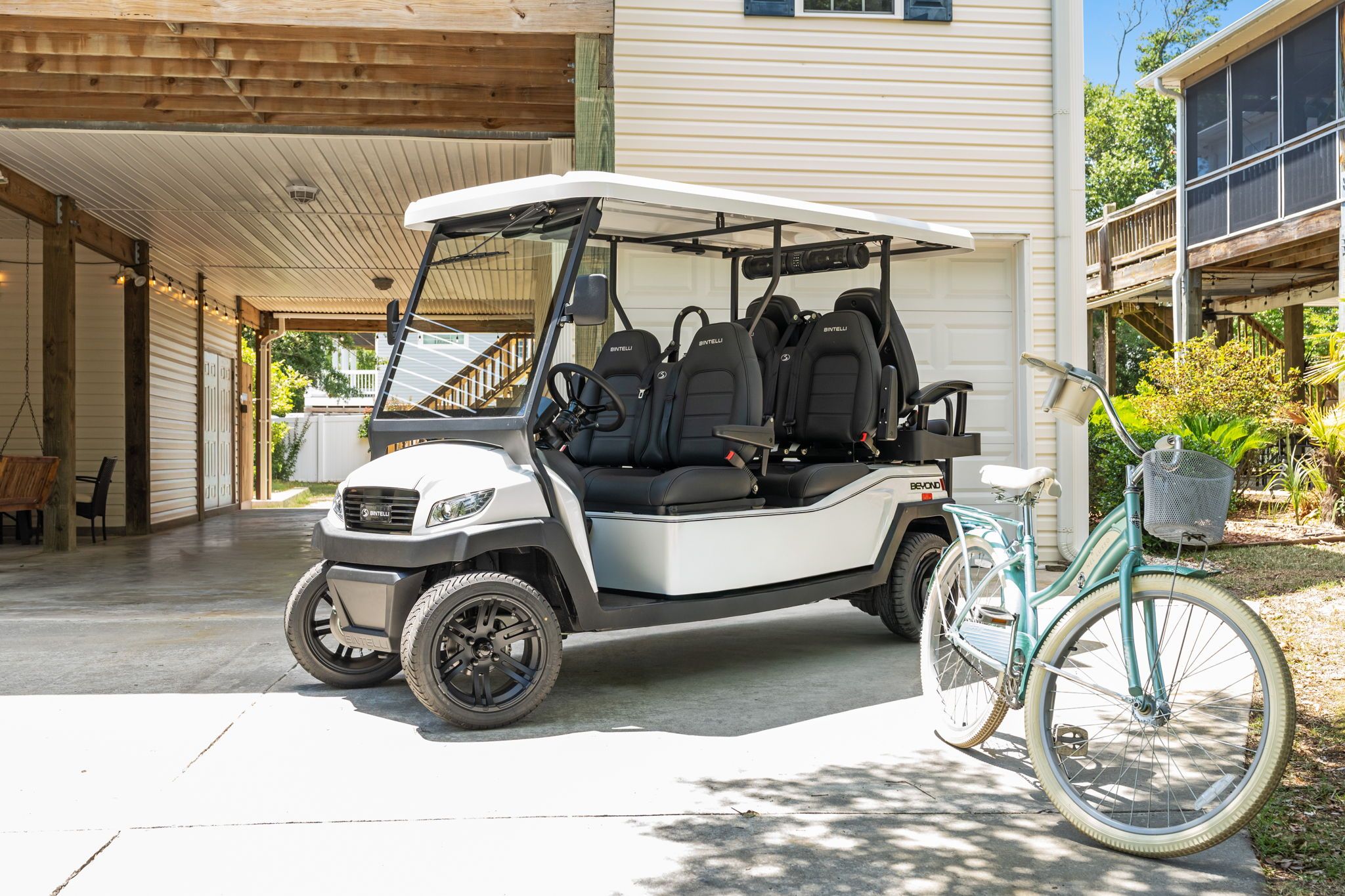 Ein Golfmobil steht in einem überdachten Außenbereich, neben einem Fahrrad und einem Korb.