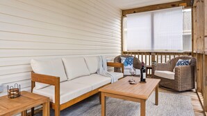 A cozy room with a wooden sofa, a wooden table, wicker chairs, and a window with blinds. - Late Summer Beach Escape | Golf Cart + Hot Tub (Oak Island)