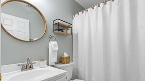 Ein Badezimmer mit weißem Waschbecken, Toilette, Spiegel und Duschvorhang.