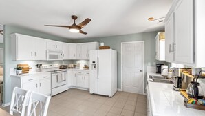 A modern kitchen with white cabinets, a microwave, oven, and a ceiling fan. - Late Summer Beach Escape | Golf Cart + Hot Tub (Oak Island)