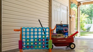 A bean bag toss game set up in a garage with a toy wagon. - Late Summer Beach Escape | Golf Cart + Hot Tub (Oak Island)