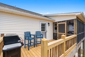 Ein überdachter Außenbereich mit Grill, zwei Stühlen und einer Holzterrasse.