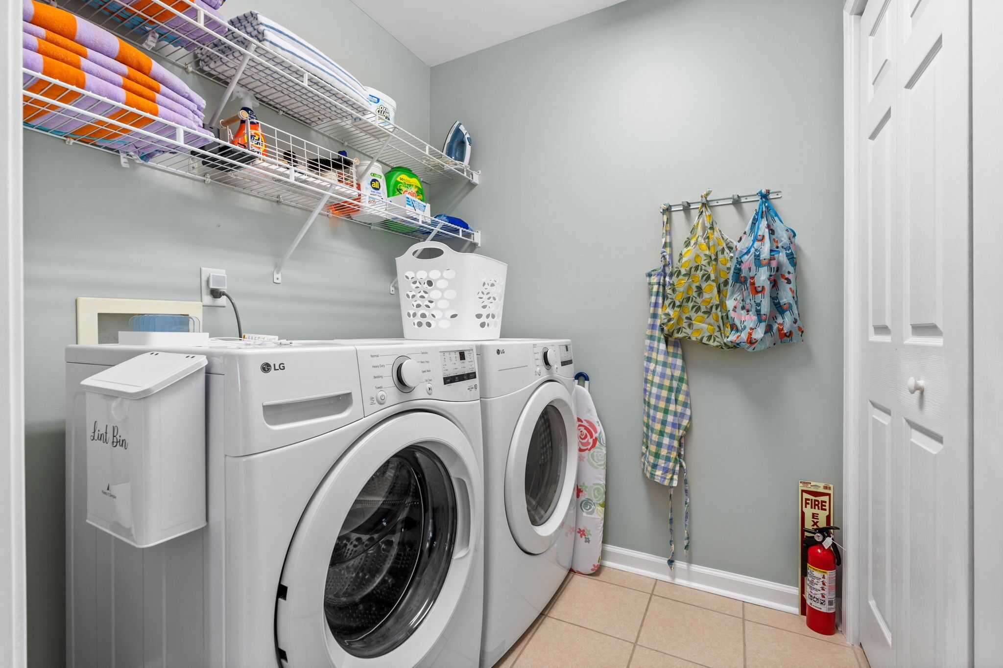 A laundry area with a washing machine, a lint bin, shelves with cleaning supplies, and a fire extinguisher.