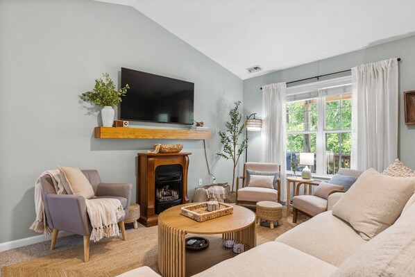 A living room with a fireplace, a television, and a large window.