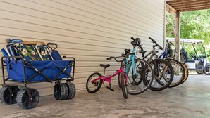 A covered parking area with a stroller, a pink bicycle, and several bicycles.
