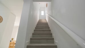Un escalier aux murs blancs, doté d’une rampe, mène à une pièce avec une fenêtre.