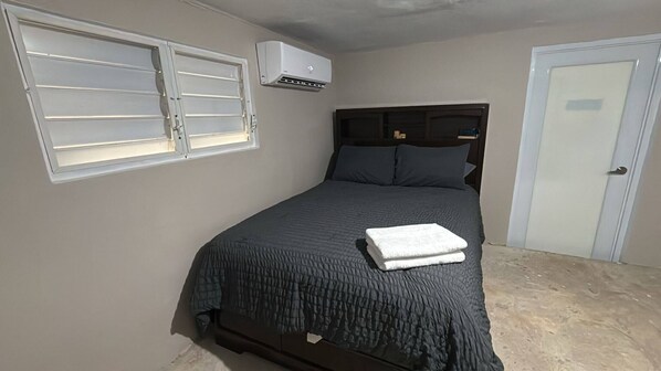 Quarto com cama, janela, ar-condicionado e porta.