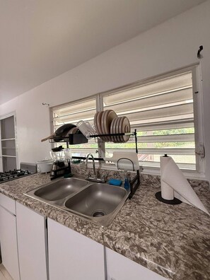 A kitchen with two sinks, a stove, a dish rack, and a window with blinds. - Walk to the Beach · BioBay & Snorkel Tours (Vieques)