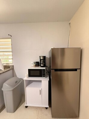 Eine kleine Küchenzeile mit Edelstahlkühlschrank, Mikrowelle und Kaffeemaschine auf einer weißen Arbeitsplatte.