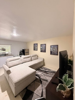 A living room with a sectional sofa, a flat-screen TV, a coffee maker, and a microwave.