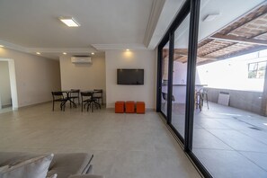 Ein geräumiges Wohnzimmer mit Flachbildfernseher an der Wand, einem Esstisch mit Stühlen und einer großen Schiebeglasdoor zum Außenbereich.