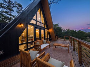 Ein modernes A-Haus mit großen Fenstern, Holzdeckmöbeln und einem Geländer mit Blick auf eine natürliche Landschaft.