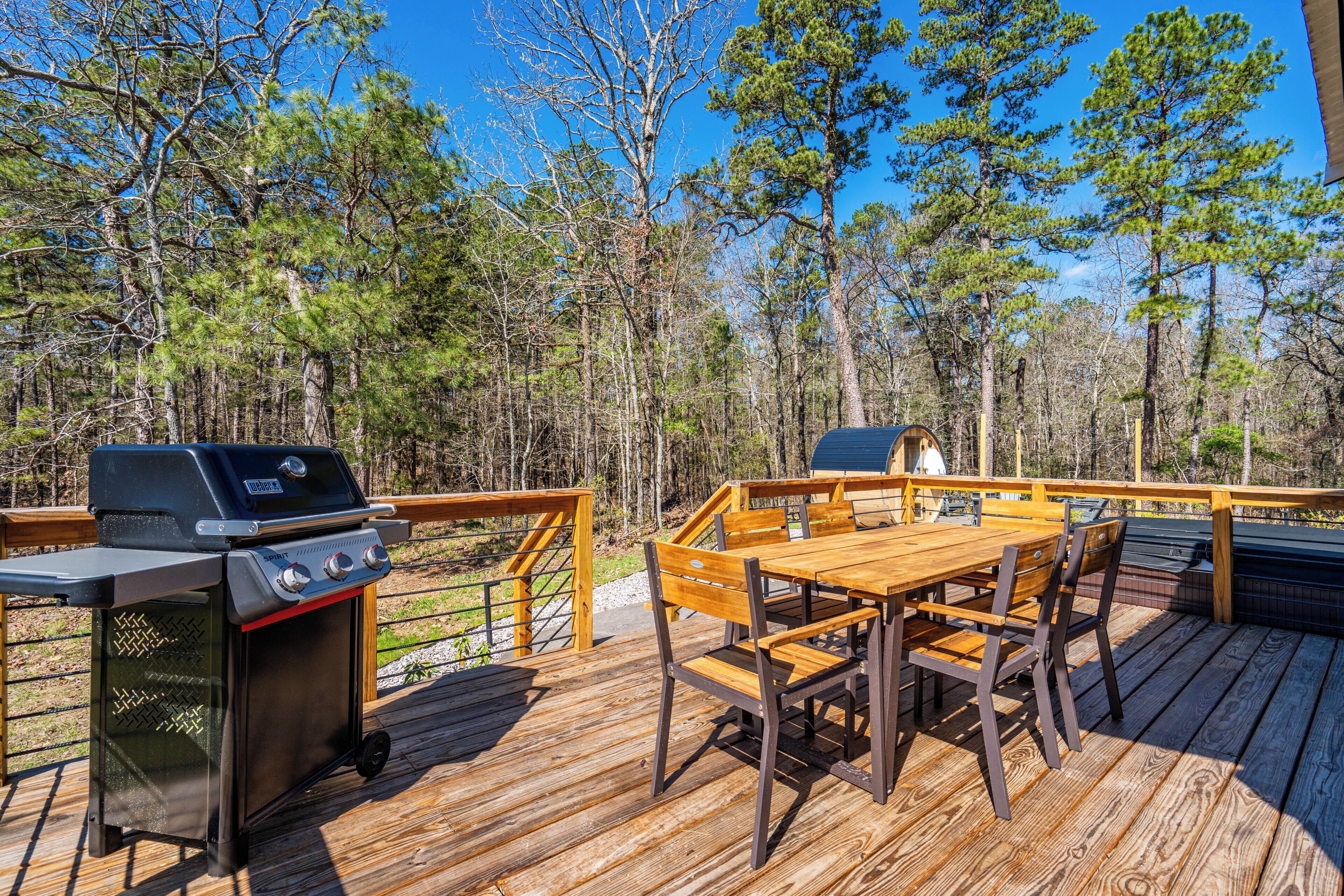 An outdoor deck with a grill, wooden table, and chairs.