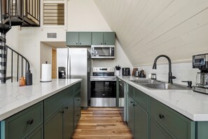 Eine moderne Küche mit grünen Schränken, Edelstahlgeräten, einer weißen Arbeitsplatte und Holzboden.