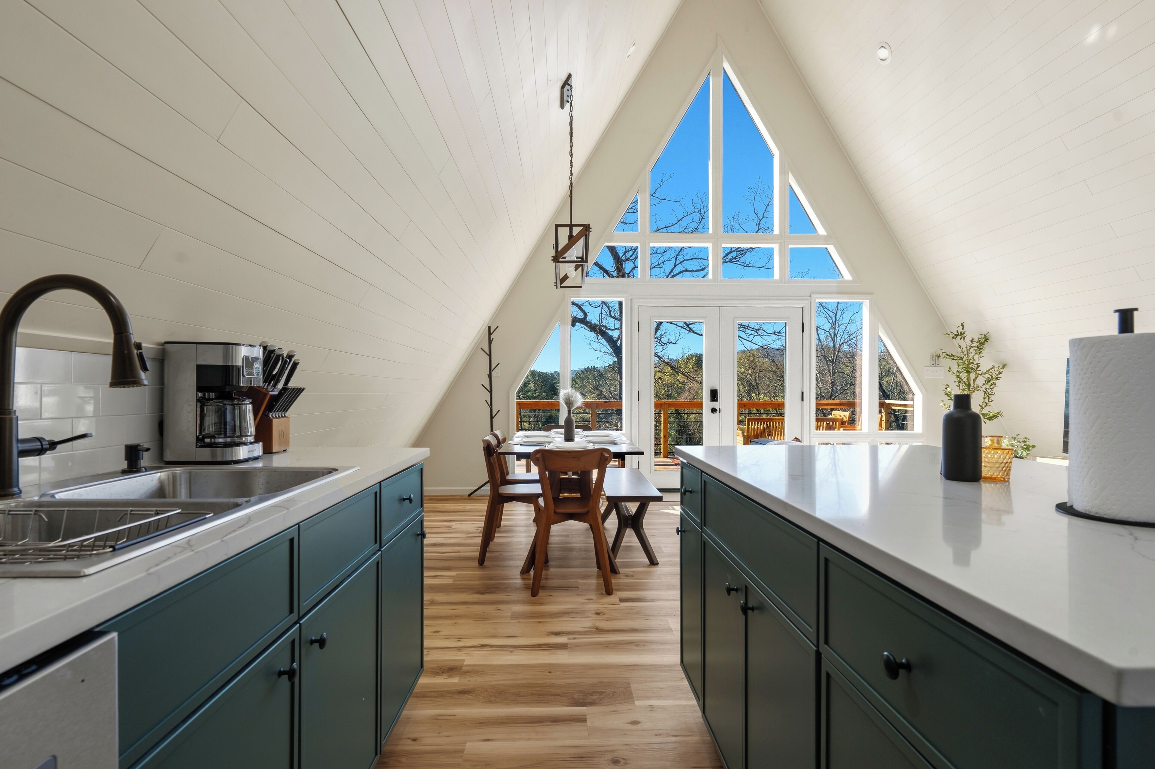 A kitchen with a dining area, wooden flooring, and a large window offering a view of trees.
