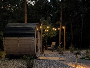 Eine Holzjagdhausartige Konstruktion, umgeben von einem Kiesweg, Bäumen und Lichterketten.