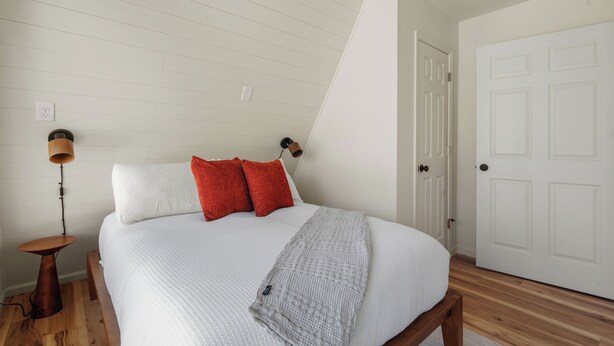 Ein Schlafzimmer mit einem Bett, einem Nachttisch, einer Lampe und einer Tür.