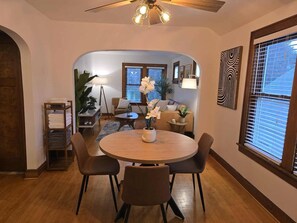 A dining area with a round table, four chairs, a ceiling fan, and a view into a living room with a sofa and a potted plant. - Whole Contemporary House in Bay View (Milwaukee)
