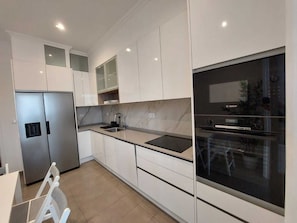 A modern kitchen with white cabinetry, a stainless steel refrigerator, a Bosch oven, and a large window.