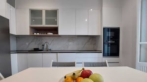 Una cocina moderna con armarios blancos, encimera de mármol y una mesa de comedor con una bandeja de fruta.
