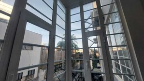 Una esquina de una habitación con ventanales amplios, una escalera visible y vistas a edificios vecinos.
