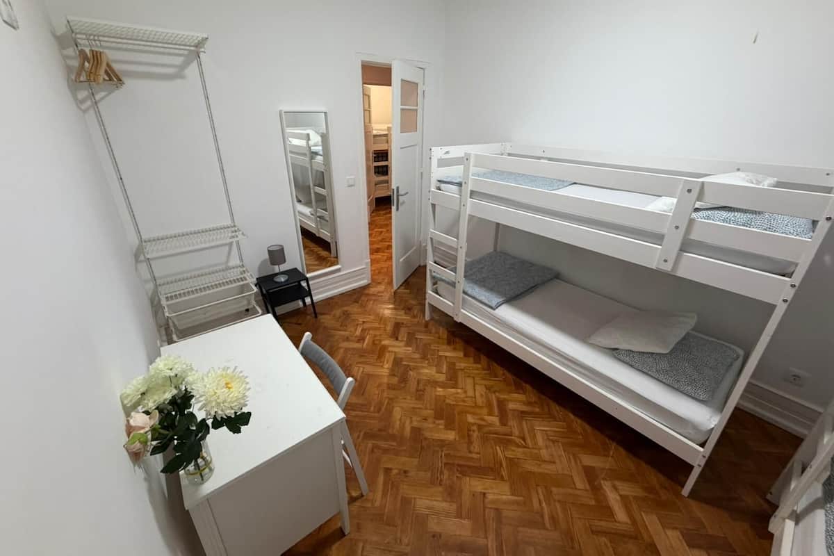 A compact room with bunk beds, a desk, a mirror, and a small closet.