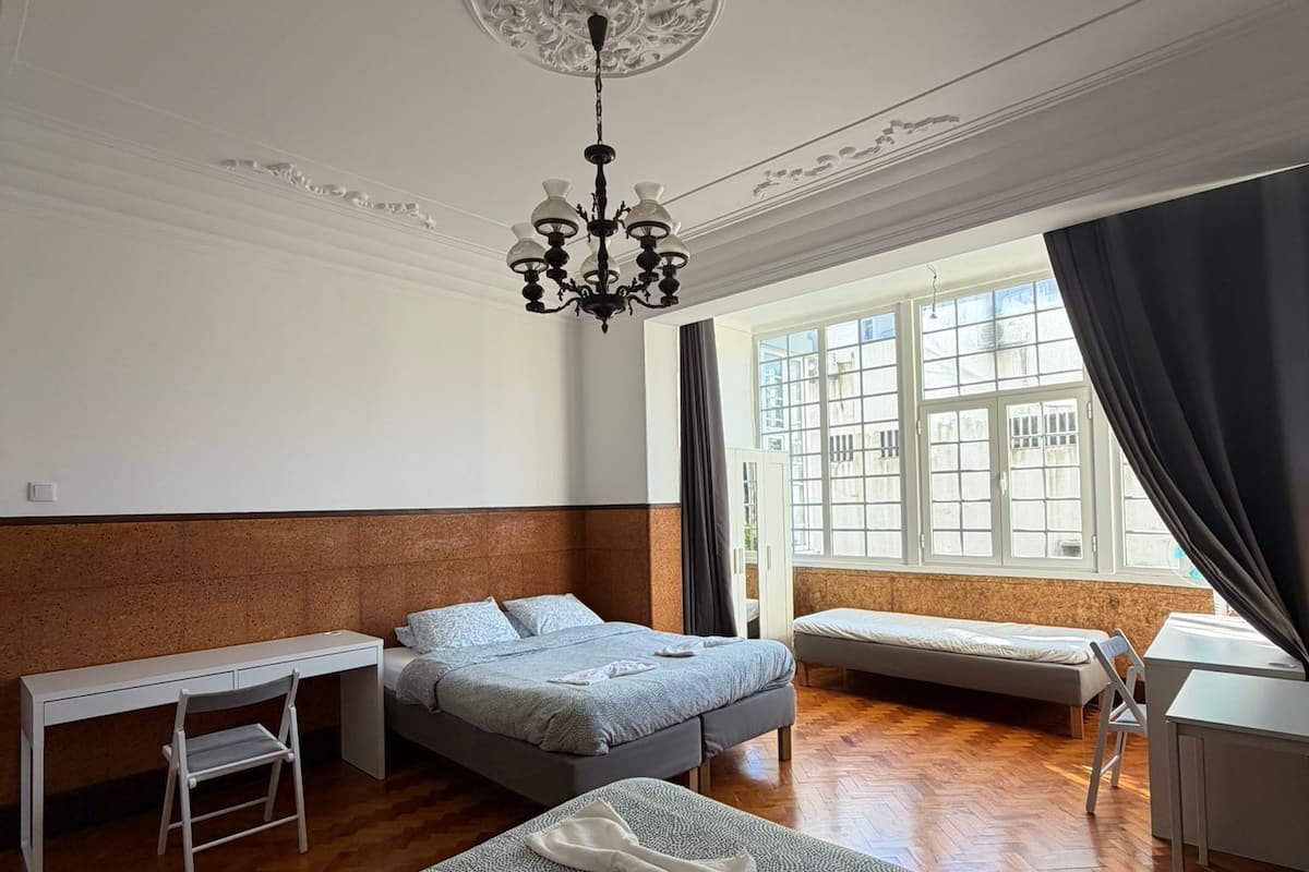 A hotel room with a large bed, a desk, a chair, a small table, and a window with curtains.