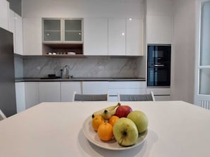 A modern kitchen with white cabinets, a marble countertop, and a dining table with a fruit plate. - Don Alvares (Lisbon)